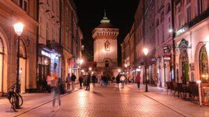 Noi Travelista - בלוג טיולים Vibrant night street scene in Krakow with St. Florian's Gate and lively pedestrian traffic.